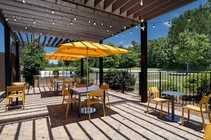 Eine Terrasse im Freien mit Backsteinböden, gelben Stühlen, einem großen gelben Sonnenschirm und Lichterketten.