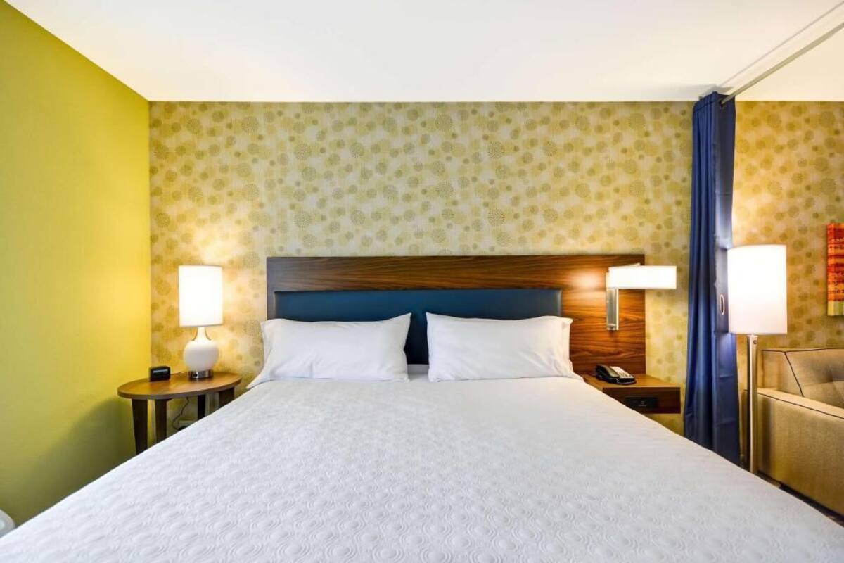 Une chambre d’hôtel avec un grand lit, deux tables de chevet avec des lampes, une tête de lit en bois et un papier peint à motifs.