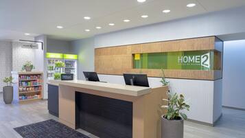 A hotel reception area with a modern design, featuring a reception desk, a refrigerator with beverages, and a vending machine.