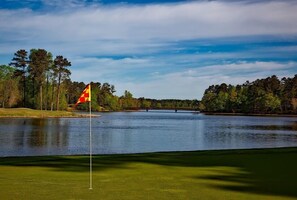 Un parcours de golf avec un drapeau sur le bloc de départ, entouré d’eau et d’arbres.