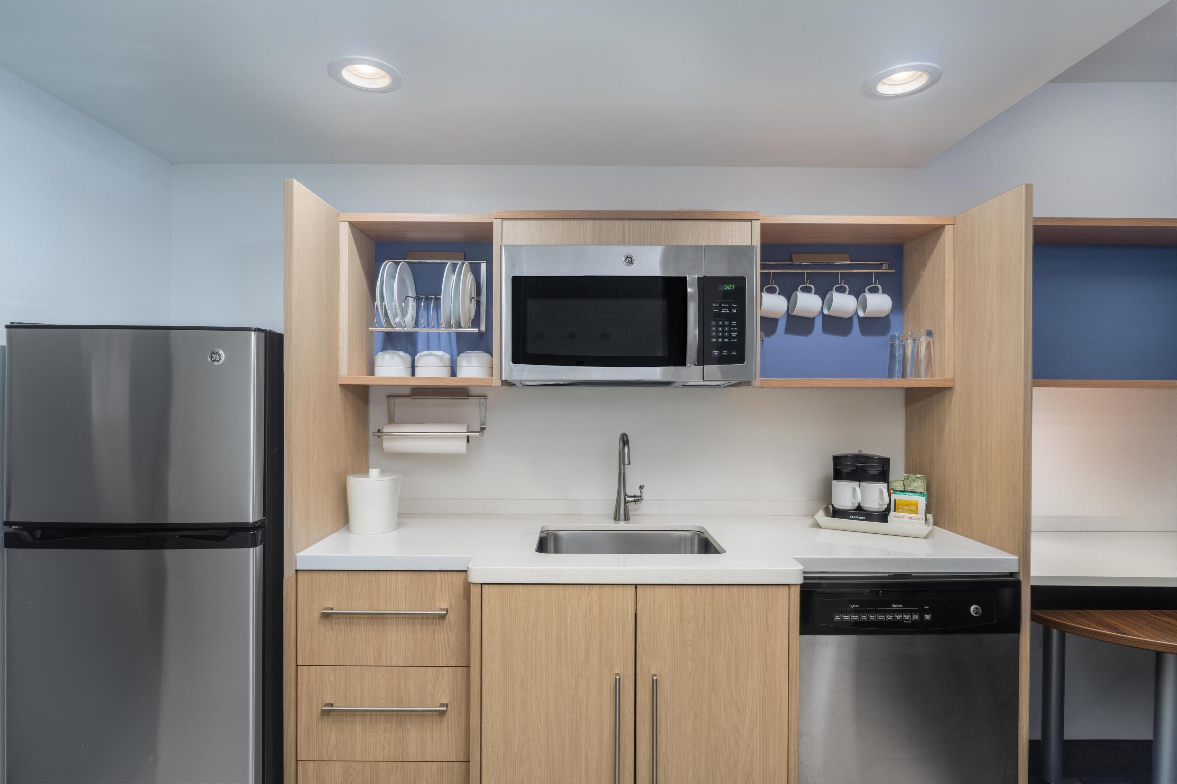 A modern kitchen with a stainless steel refrigerator, a microwave, a dishwasher, and wooden cabinets.