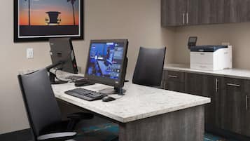 A hotel room with a desk, two chairs, a computer, and a printer.