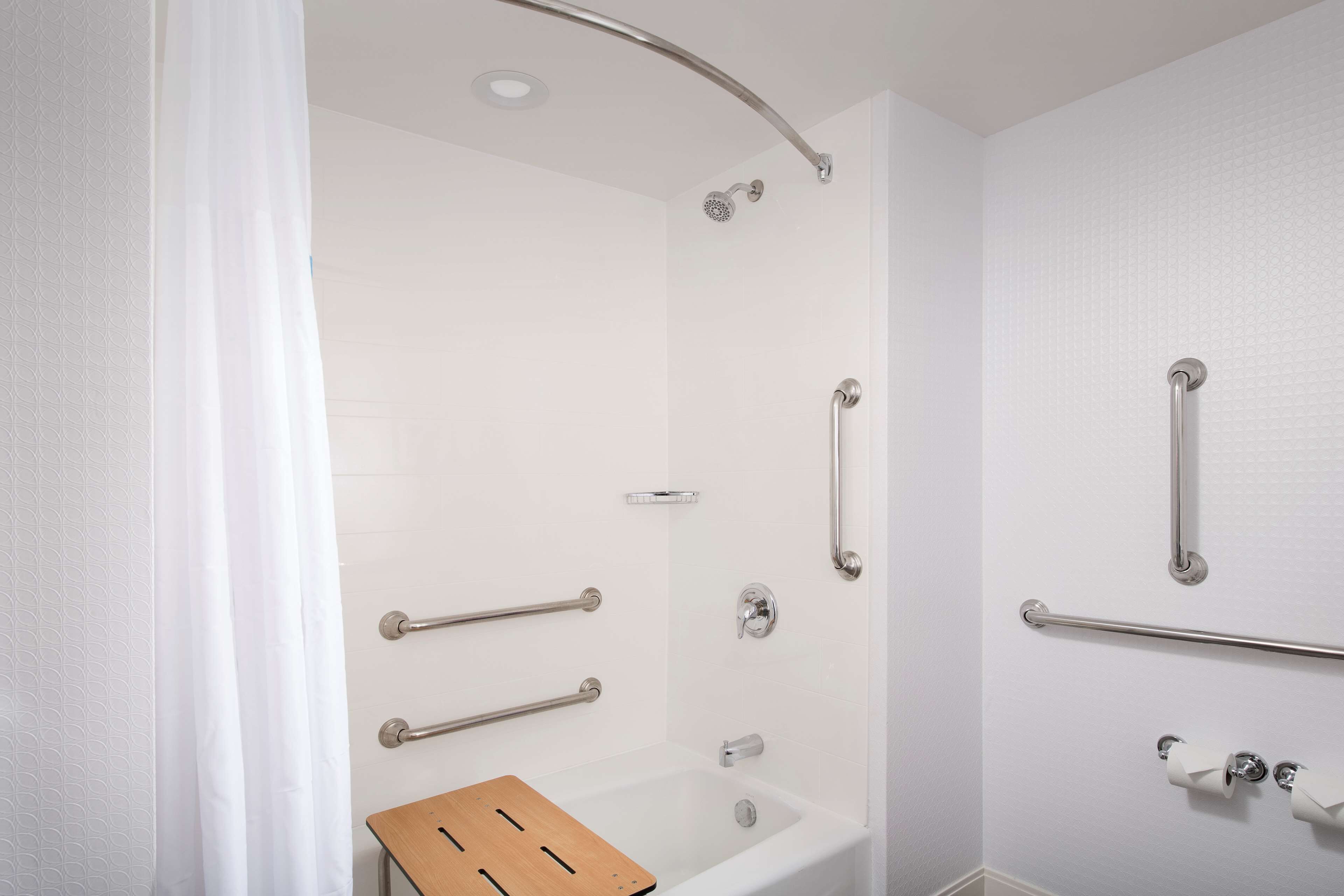 A modern bathroom with a shower, grab bars, and a wooden bath mat.