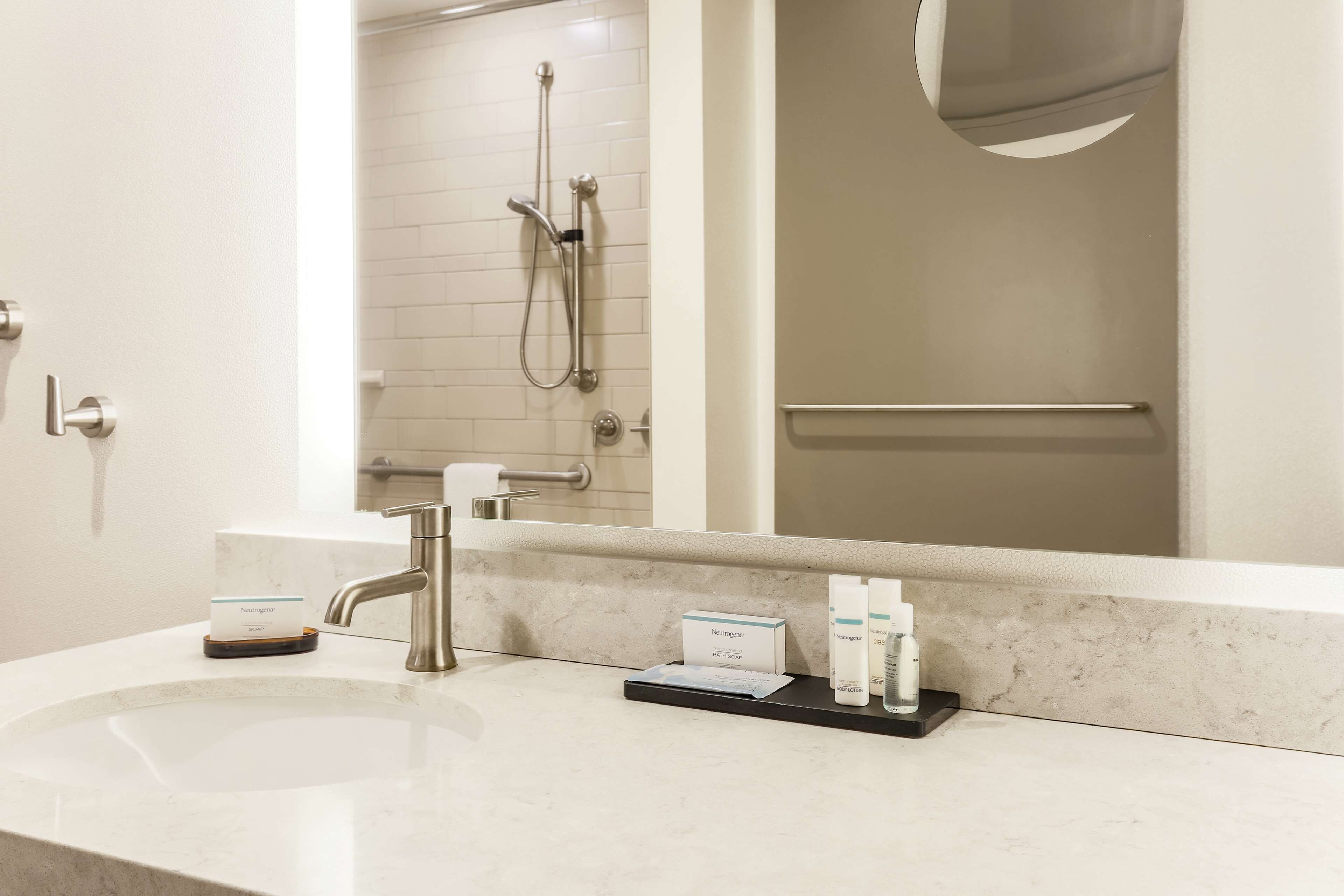 A hotel bathroom with a sink, mirror, and toiletries.