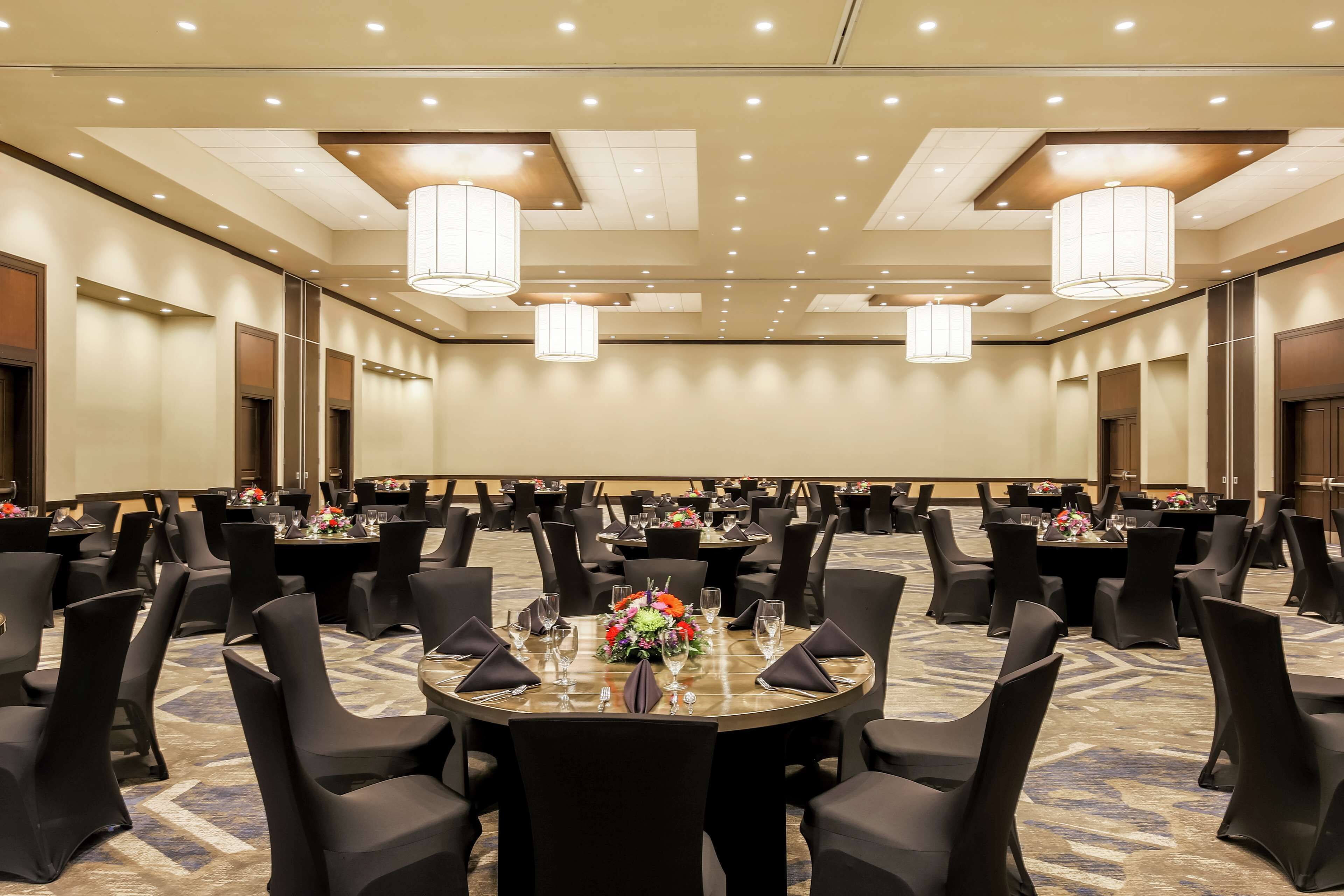 A conference room with round tables, black chairs, and chandeliers.