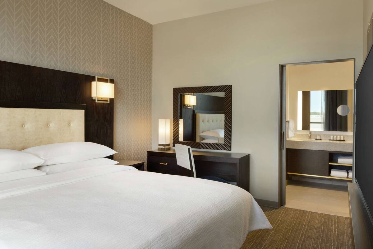 Een hotelkamer met een groot bed, een bureau met stoel, een spiegel en een inloopkast.