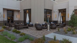 Een terras met rieten meubilair en parasols, omgeven door een aangelegde tuin met grind en beplanting.