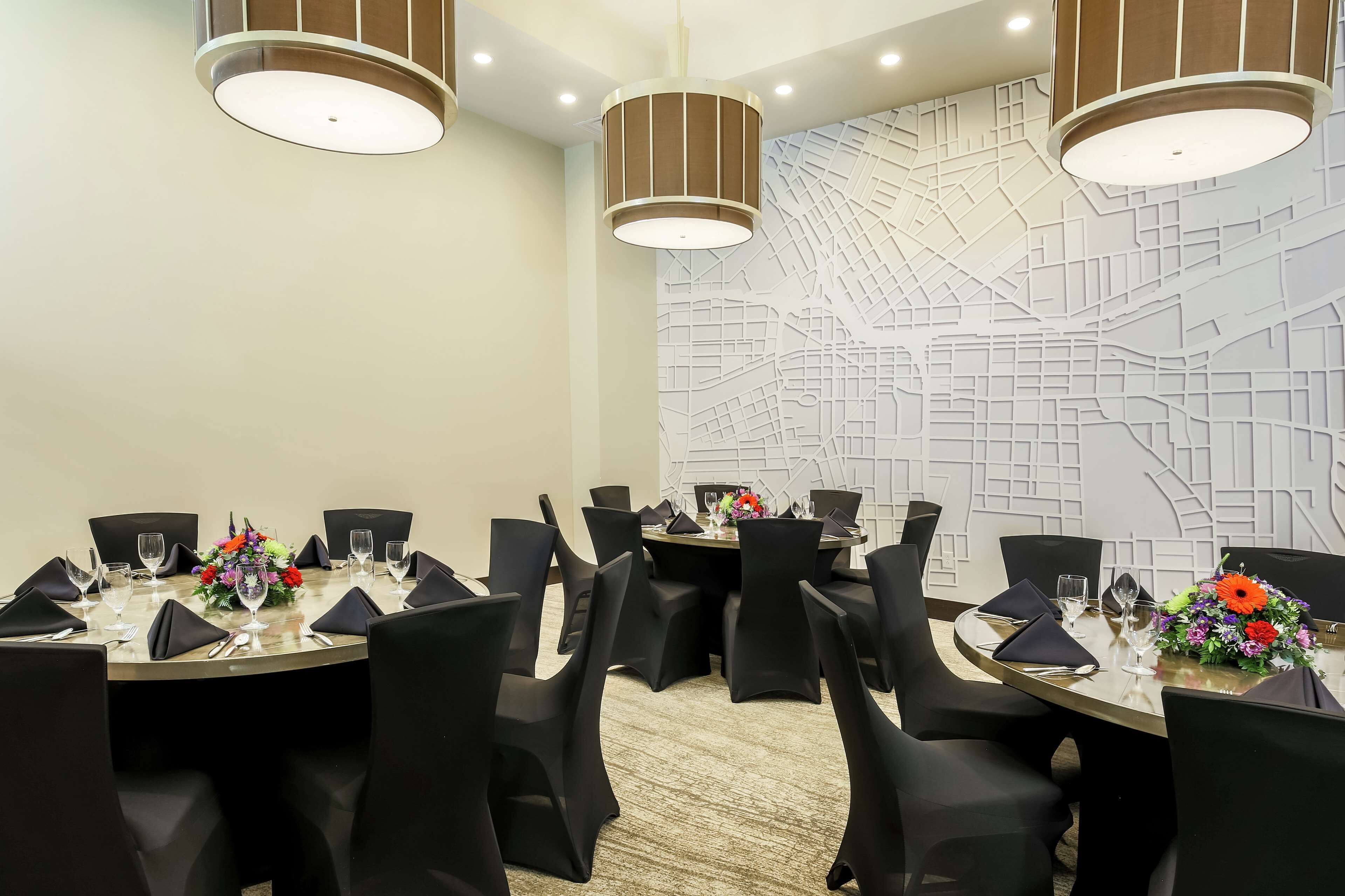 Un salón de conferencias con mesas redondas, sillas negras y centros de mesa con flores.