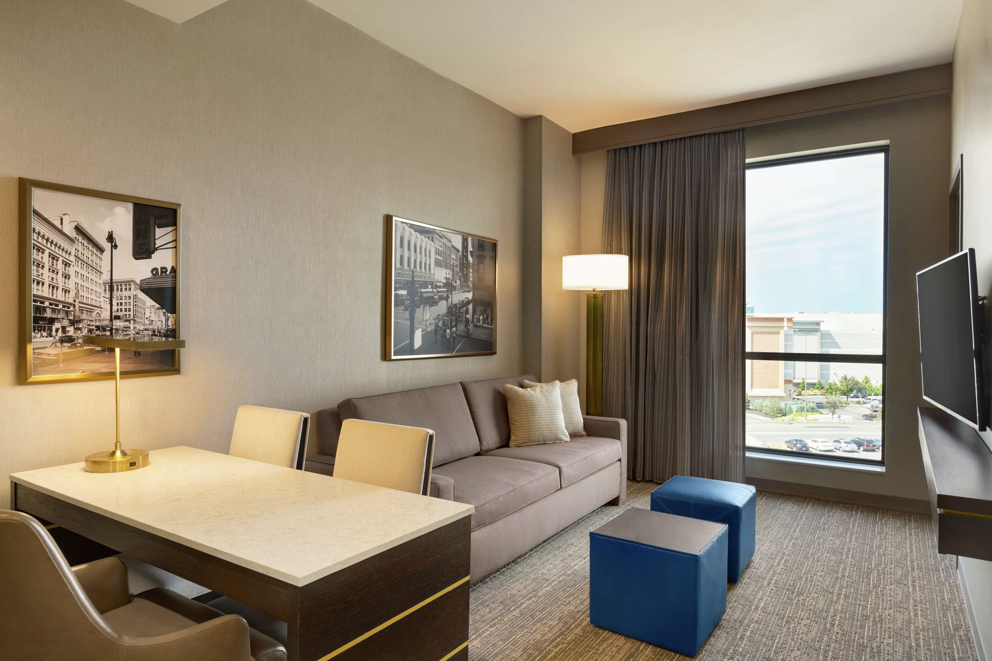 Une chambre d’hôtel avec un canapé, un bureau avec une lampe, une télévision et une grande fenêtre donnant sur la ville.