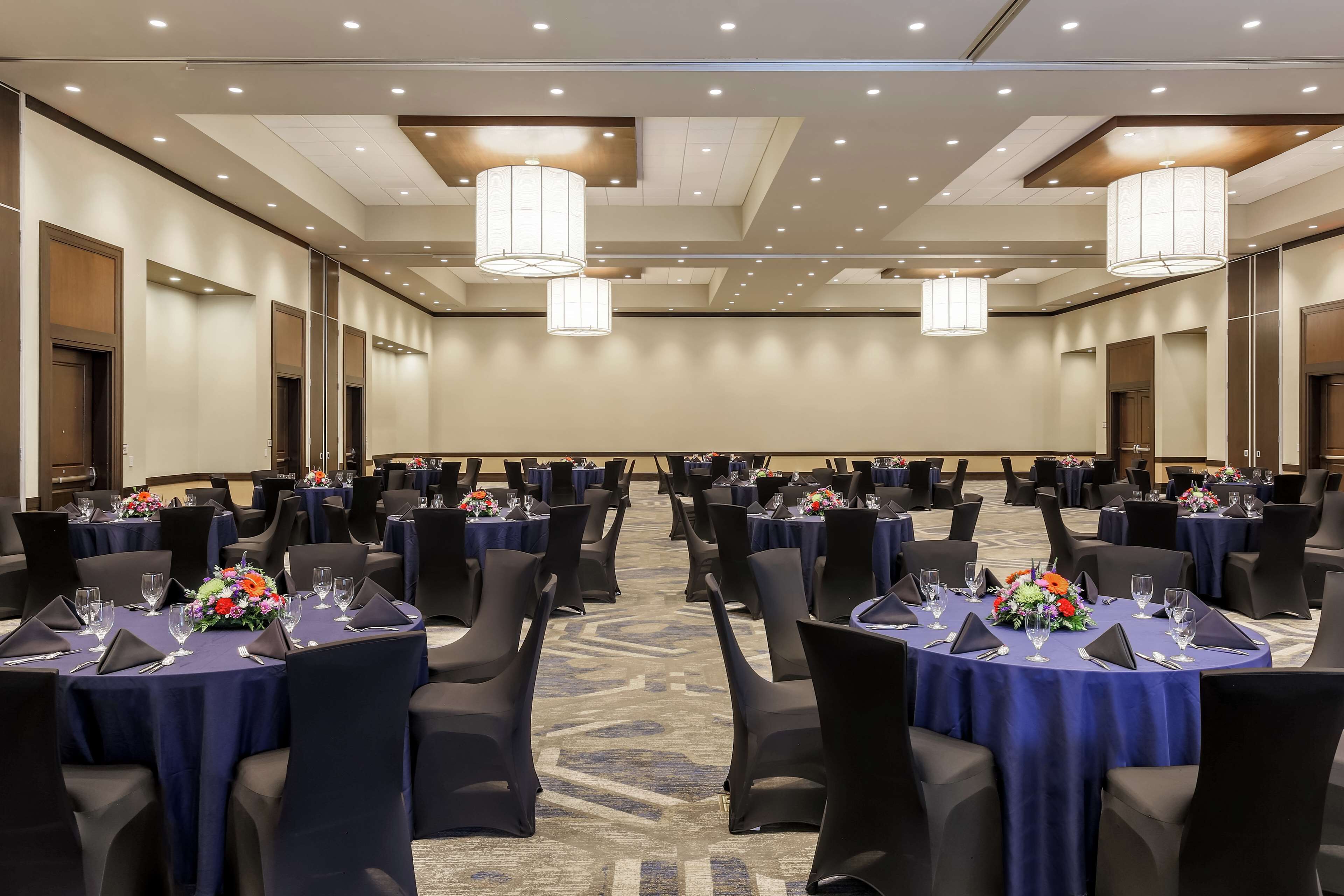 Un salón de conferencias con mesas redondas, sillas negras y centros de mesa florales.