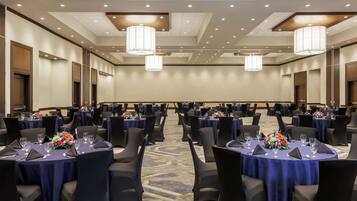 Un salón de conferencias con mesas redondas, sillas negras y centros de mesa florales.