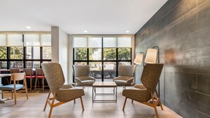 A modern lounge area with two armchairs, a small table, and a dining table with chairs. Large windows provide a view of the outdoors.