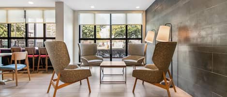 A modern lounge area with two armchairs, a small table, and a dining table with chairs. Large windows provide a view of the outdoors.