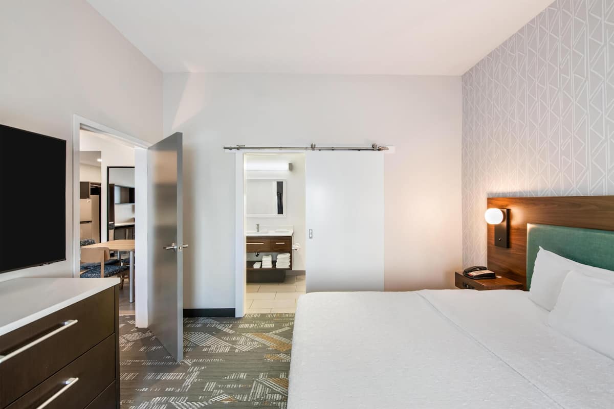 Ein Hotelzimmer mit Bett, Schminktisch, Fernseher, Kleiderschrank und einem durchgegangenen Tür sichtbar liegenden Badezimmer.