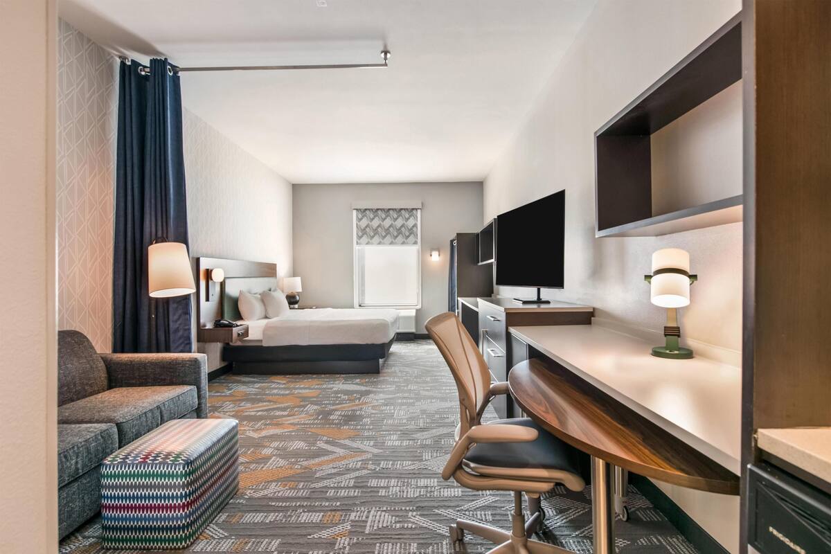 Ein Hotelzimmer mit einem Bett, einem Schreibtisch, einem Sessel, einer Couch, einem kleinen Tisch und einem gemusterten Teppich.