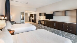 A hotel room with two beds, a desk, a TV, and a minibar.