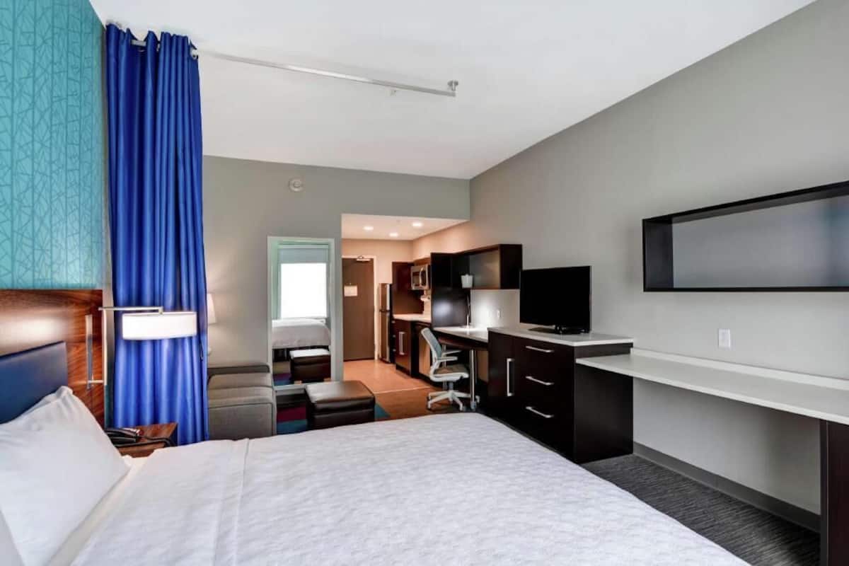 Ein Hotelzimmer mit Bett, Schreibtisch, Fernseher und einer Küchenzeile.