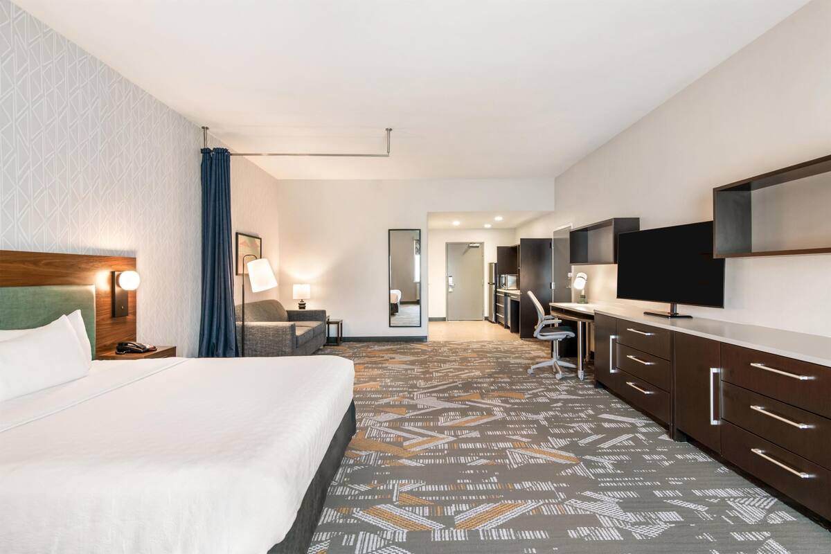 Ein Hotelzimmer mit einem großen Bett, einem Schreibtisch, einem Fernseher und einem Badezimmer im Hintergrund.