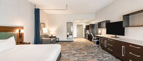 A hotel room with a large bed, a desk, a television, and a bathroom visible in the background.