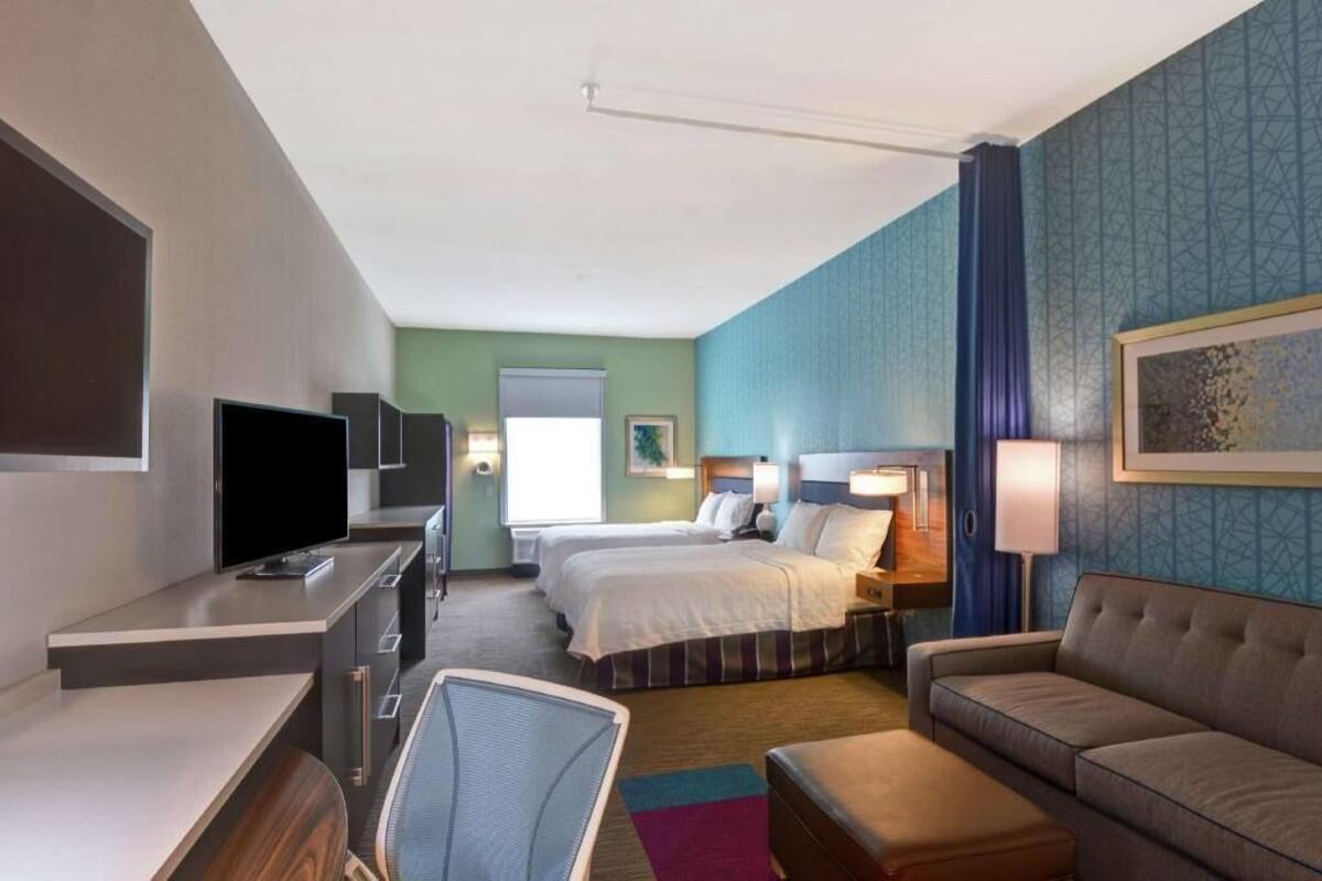 Ein Hotelzimmer mit Bett, Schreibtisch mit Fernseher, einer Couch und einem Sessel.