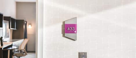 Een hotelkamer met een nummerbord aan de muur, een bureau met stoel en een televisie.