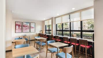 A modern dining area with tables and chairs, large windows with a view of greenery, and framed artwork on the walls.