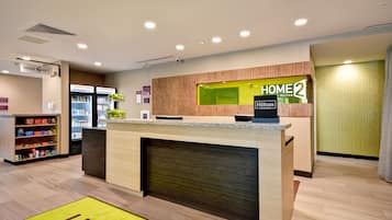 A hotel reception area with a wooden reception desk, a digital display, and a self-service kiosk.