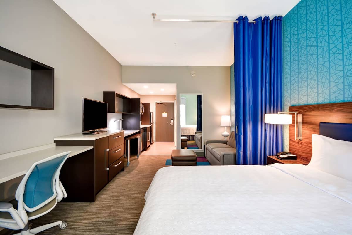 Une chambre d’hôtel équipée d’un lit, d’un bureau, d’une chaise, d’une télévision et donnant sur le couloir.