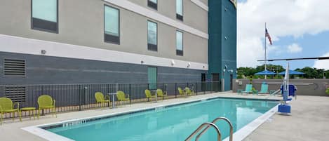 A swimming pool with a metal ladder, green chairs, and a flagpole with an American flag.