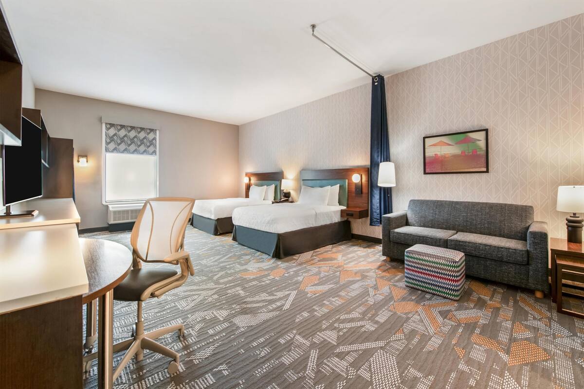 Ein Hotelzimmer mit einem Bett, zwei Nachttischen, einem Schreibtisch, einem Sessel und einem gemusterten Teppich.