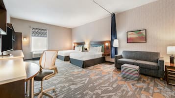 A hotel room with a bed, two bedside tables, a desk, a chair, a sofa, and a patterned carpet.