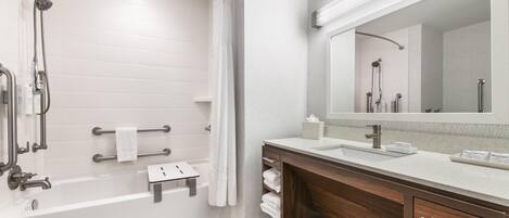 Un baño moderno con ducha a nivel, tocador con espejo y bañera.