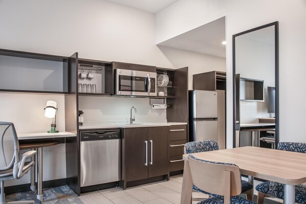 A compact kitchen with modern appliances, a dining area with patterned chairs, and a built-in mirror.