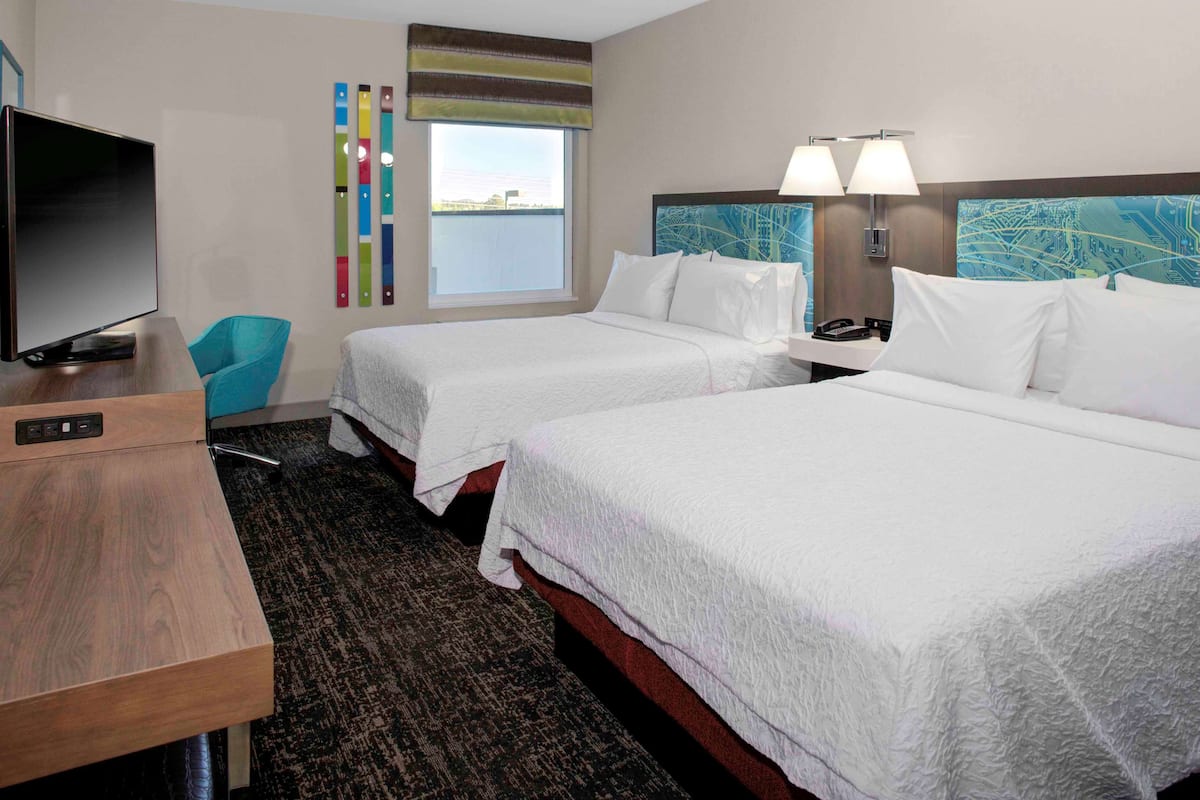 A hotel room with two beds, a TV, a desk, and a view of the water.