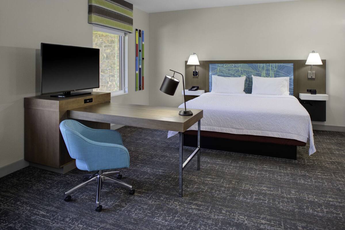 A hotel room with a bed, a desk with a TV, a chair, and two bedside lamps.