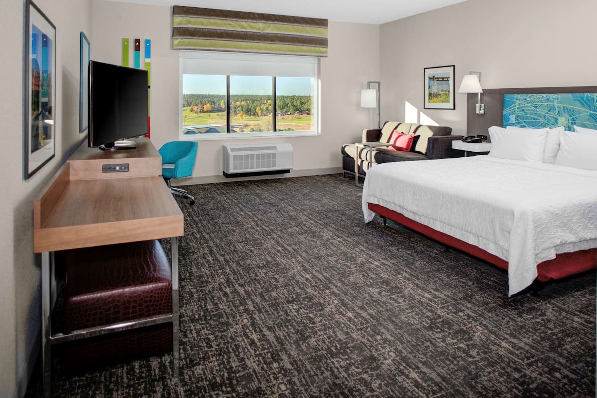 A hotel room with a bed, a desk, a TV, a chair, and a window with a view of the outdoors.