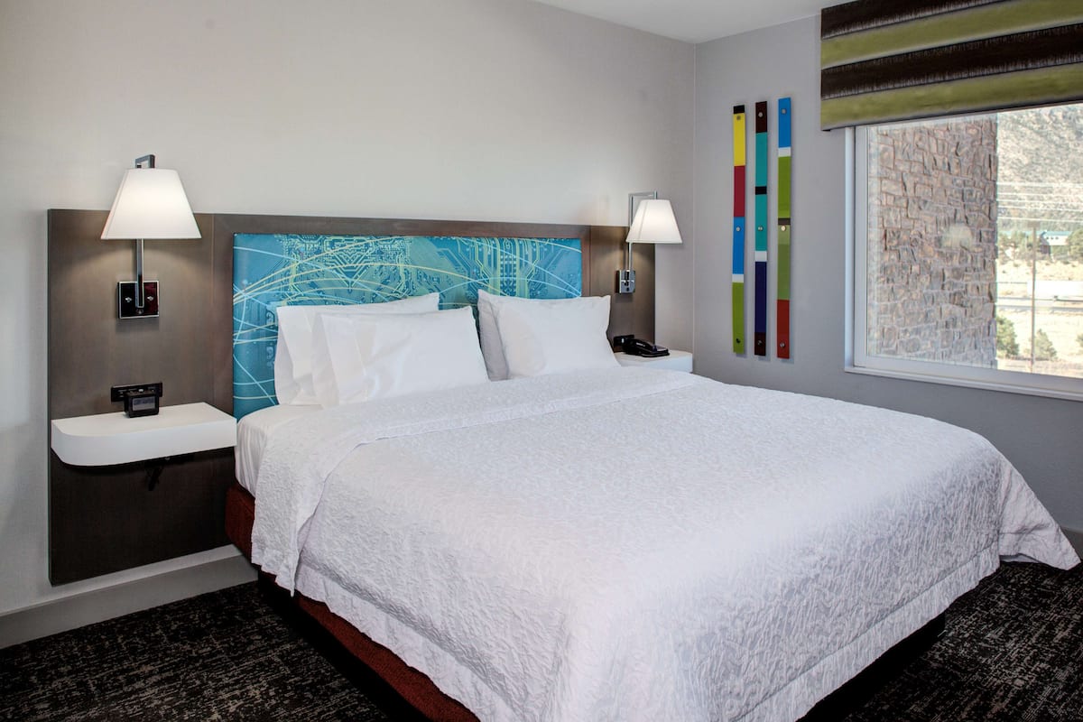 A hotel room with a large bed, two bedside tables with lamps, a wall-mounted phone, and a window with a view of the outside.