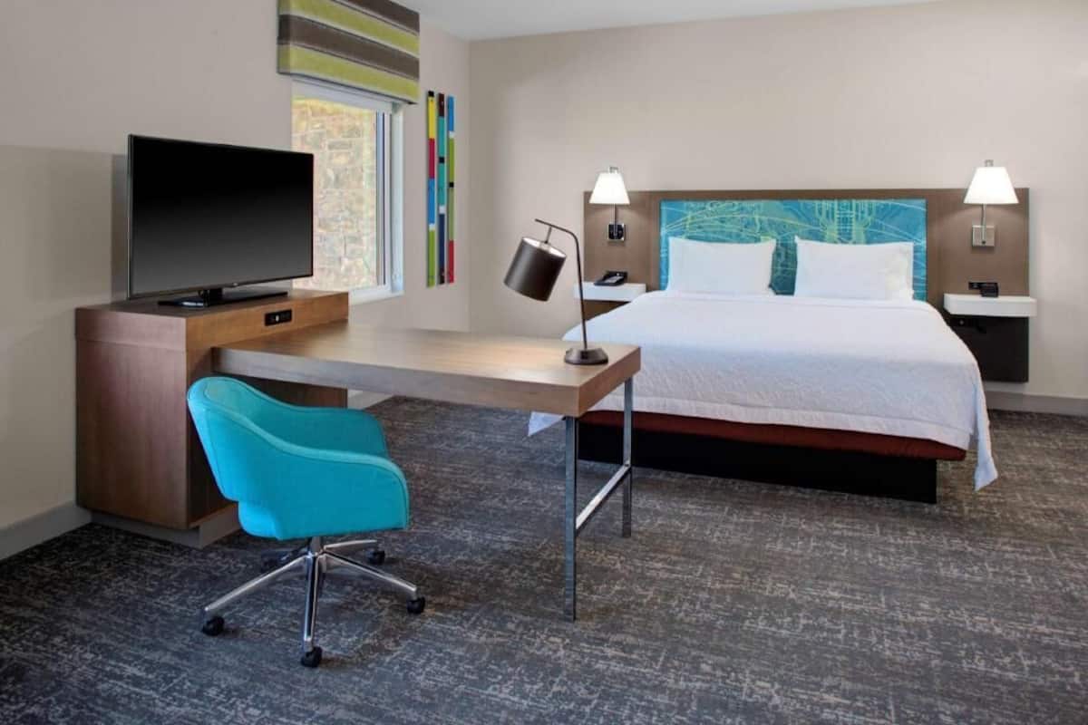 A hotel room with a bed, a desk with a TV, a chair, and two bedside lamps.