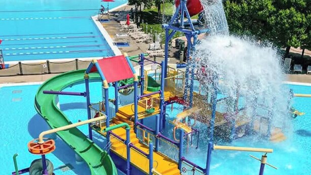 Ein Wasserpark mit einer grünen Rutsche, einer Wasserstrahl-Attraktion und einem Poolbereich.