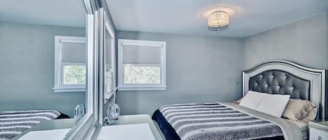 A bedroom with a large mirror, a bed with a tufted headboard, bedside tables, and a small window.