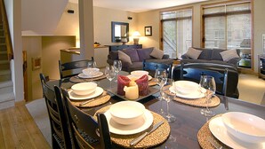 Un comedor con una mesa de madera dispuesta para cuatro, rodeada de sillas. Hay platos, vasos y una vela sobre la mesa.