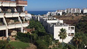 Zona residencial costeira com edifícios modernos, incluindo um edifício de vários andares com varandas e um prédio com telhado plano e antenas parabólicas.