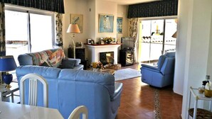 Uma sala de estar com sofá, cadeiras, televisão e lareira.