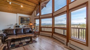 Un vaste salon doté d’un plafond en bois, de grandes fenêtres offrant une vue sur un paysage désertique, d’un canapé en cuir et d’une table basse rustique.
