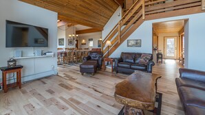 Un vaste espace de vie doté d’un plafond en bois, d’un escalier et d’un téléviseur à écran plat fixé au mur.