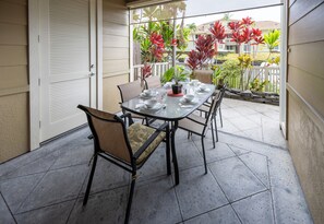 A covered outdoor dining area with a table set for four, surrounded by chairs with cushioned seats.
