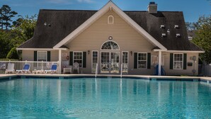 A pool area with a building that has a gabled roof, a large arched entrance, and a clock above the door. There are lounge chairs and a sign that says "No Lifeguard on Duty." - Beautiful Large Two Story Condo Near The Beach With Unique Pricing! (North Myrtle Beach)