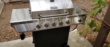A stainless steel grill with four burners and a side shelf, placed outdoors on a concrete surface.