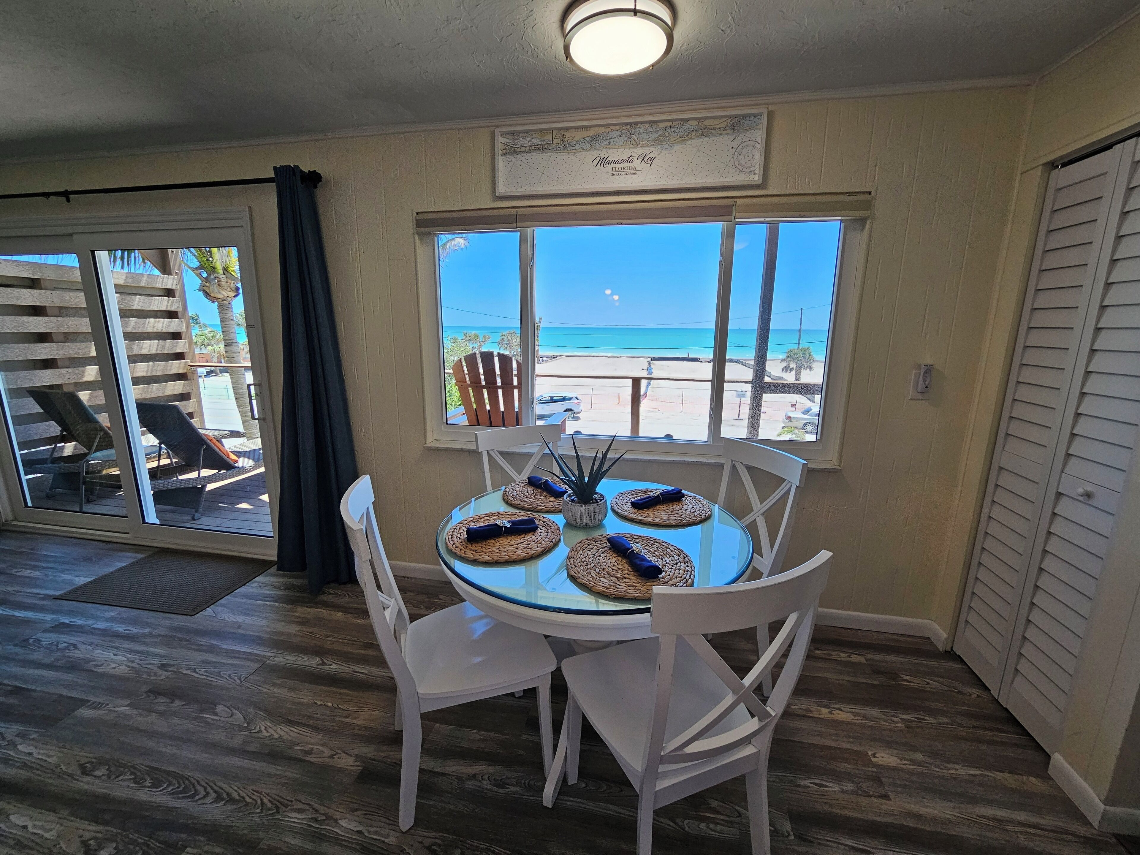 A dining area with a glass table, white chairs, and a view of the beach.