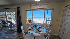 Un comedor con una mesa de vidrio, sillas blancas y vistas a la playa.